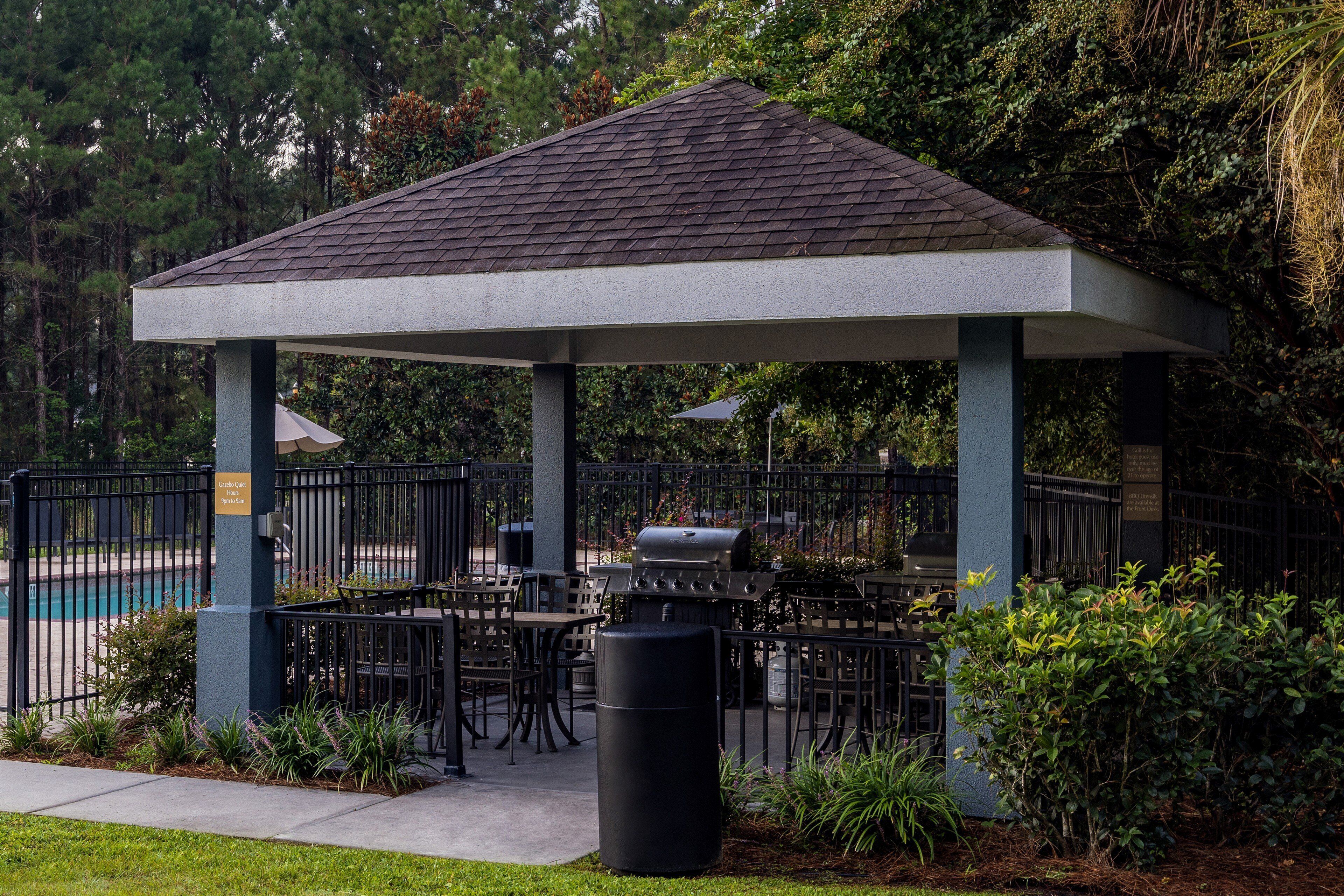 Un kiosque doté d’un toit en tuiles, entouré d’une clôture, et comprenant un espace salon extérieur et un barbecue.