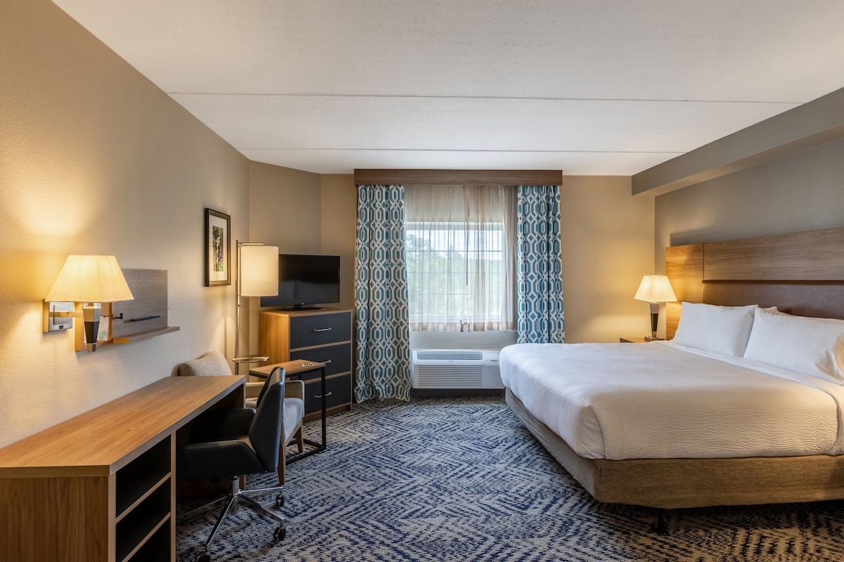 A hotel room with a bed, desk, chair, TV, and a window with curtains.