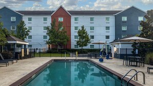 A swimming pool with a brick border, surrounded by outdoor seating and a building with multiple windows in the background. - Candlewood Suites Bluffton-Hilton Head by IHG (Bluffton)