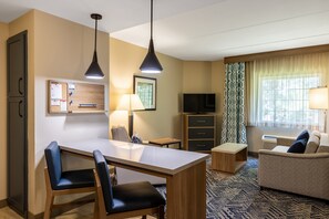 Une chambre d’hôtel comprenant un coin repas, un canapé, une télévision, un bureau et un tableau d’affichage.