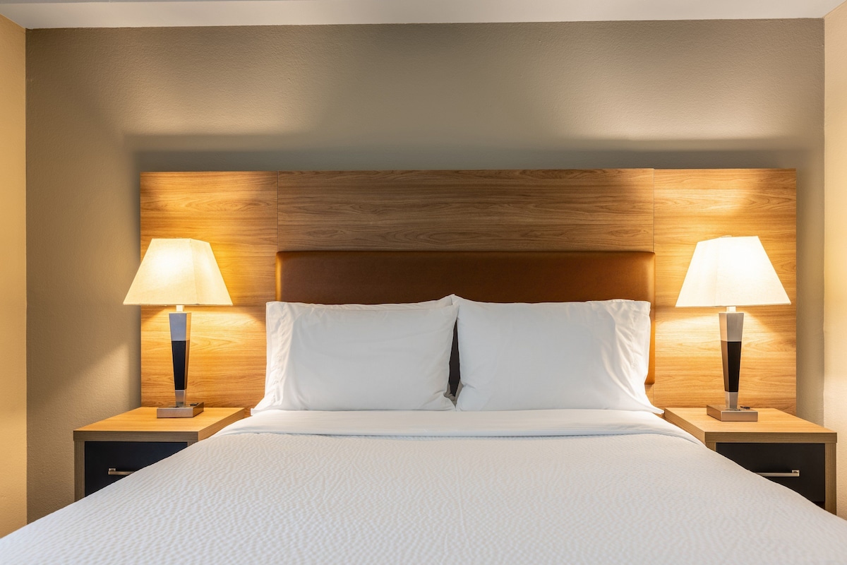 A neatly made bed with white linens, flanked by two bedside tables with lamps, set against a wooden headboard.