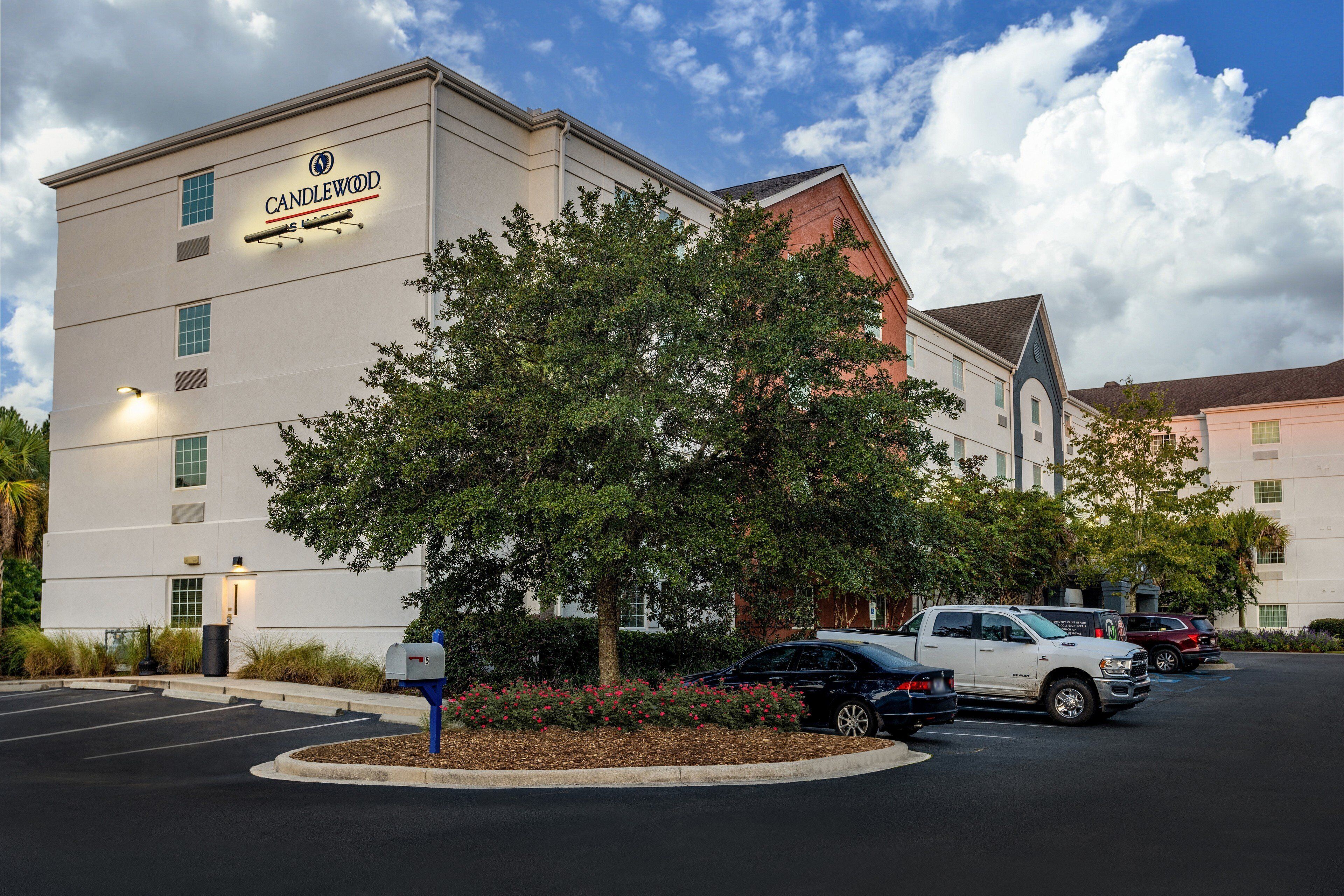 A hotel with a sign reading "CANDLEWOOD" and a parking lot with several cars.