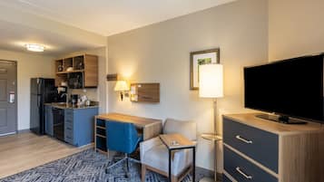Una habitación de hotel compacta con kitchenette, televisor de pantalla plana, escritorio con silla y alfombra estampada.