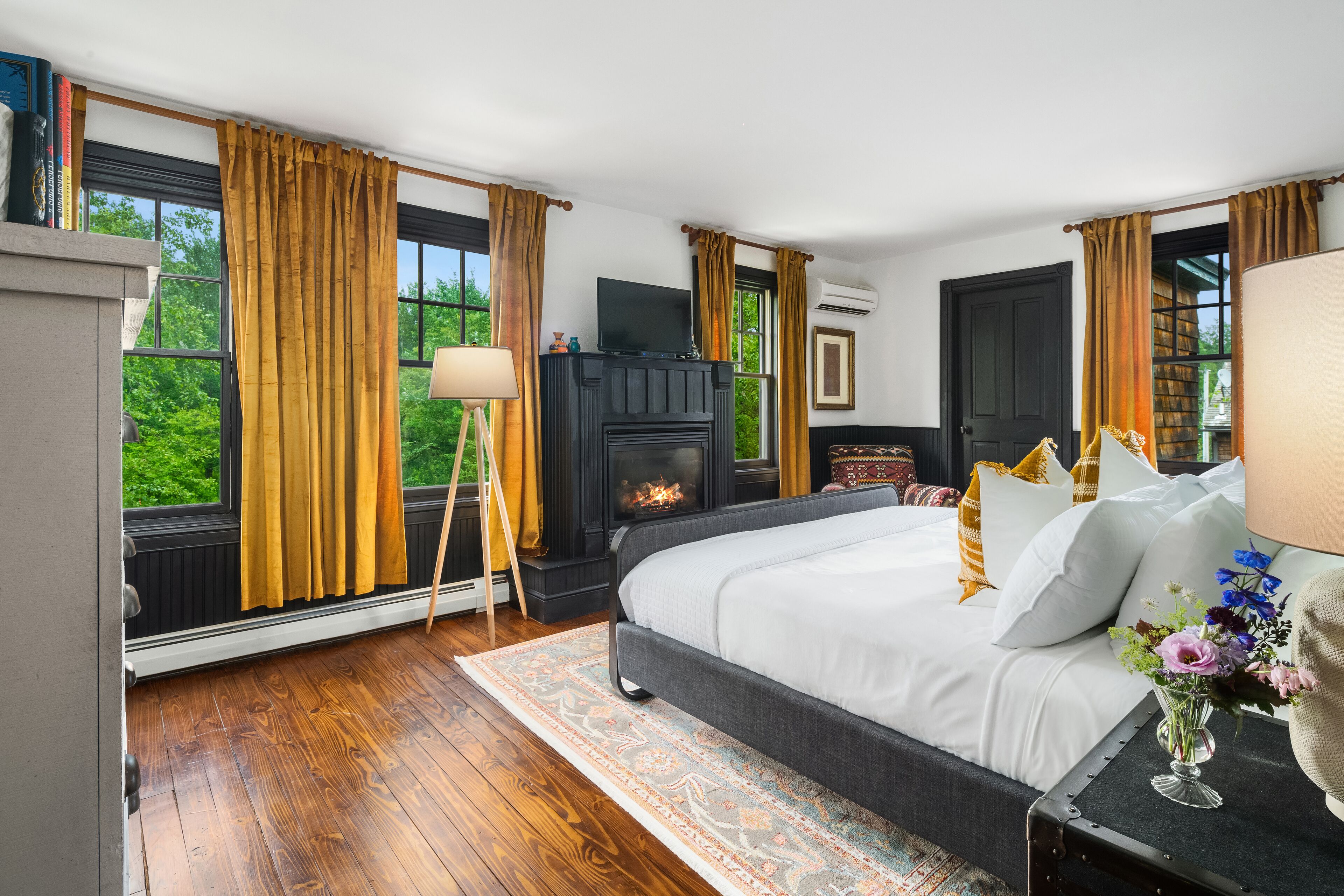 Un dormitorio con chimenea, ventanas amplias y cama con ropa blanca.
