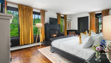Un dormitorio con chimenea, ventanas amplias y cama con ropa blanca.