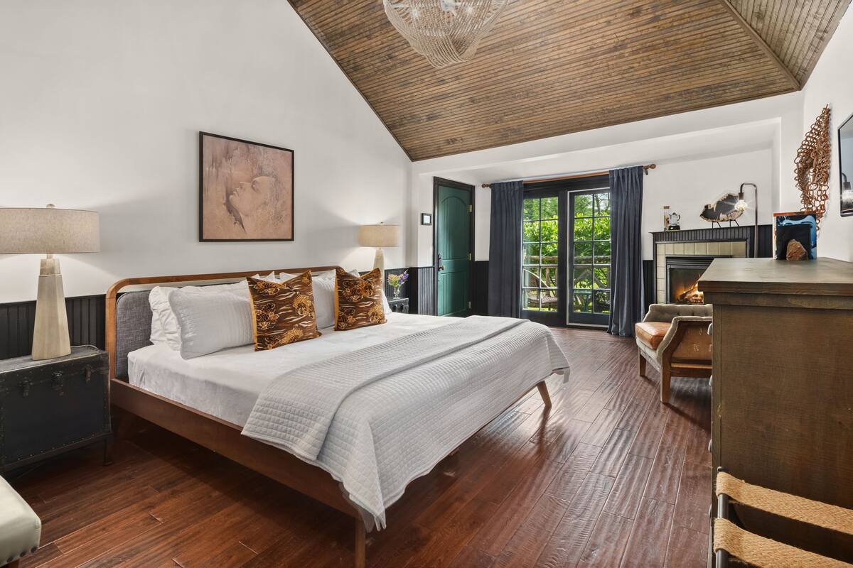 A spacious bedroom with a large bed, wooden floor, and a view of the outdoors.