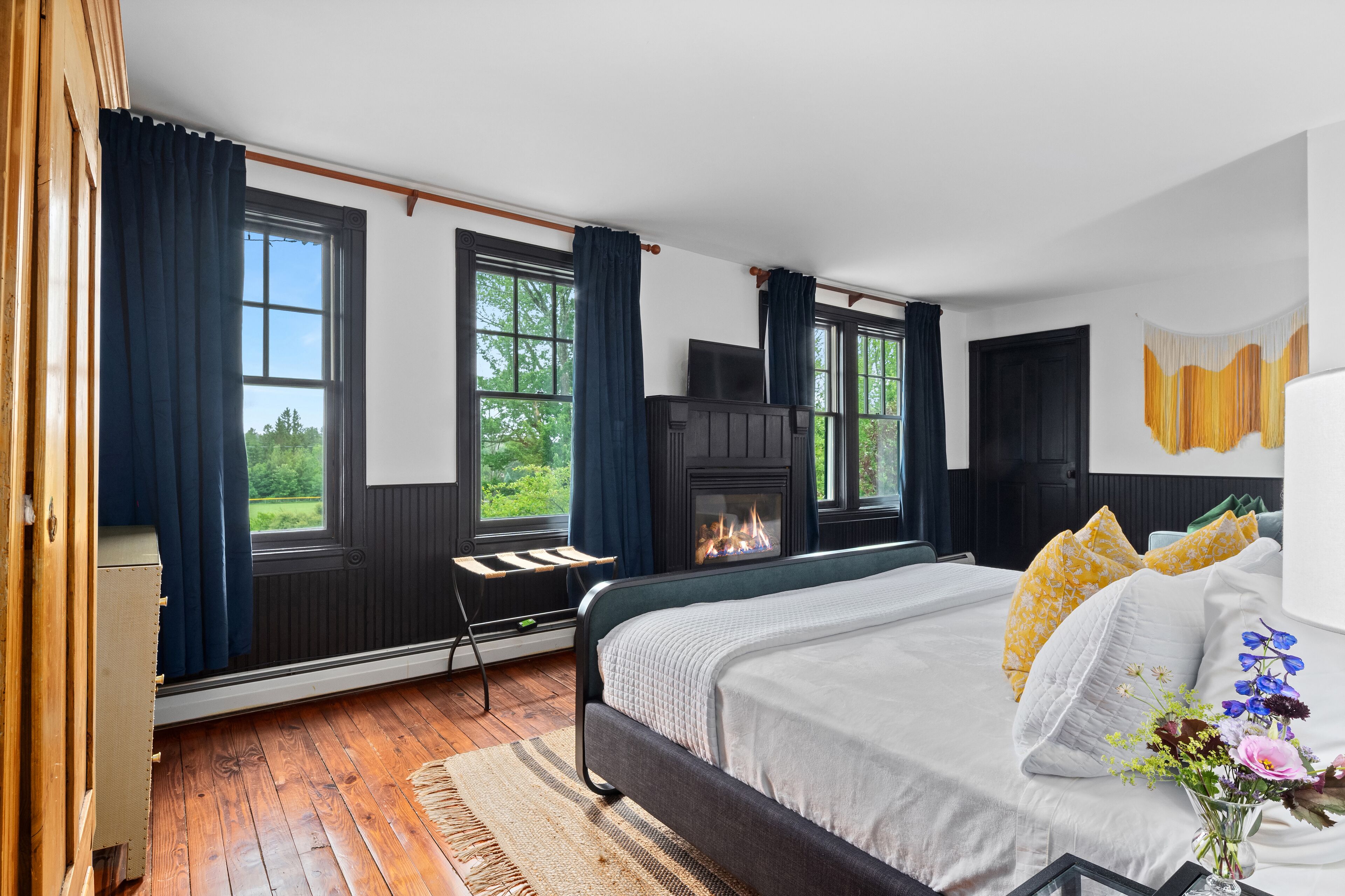 Un dormitorio con una cama grande, una chimenea y vistas a zonas verdes a través de las ventanas.