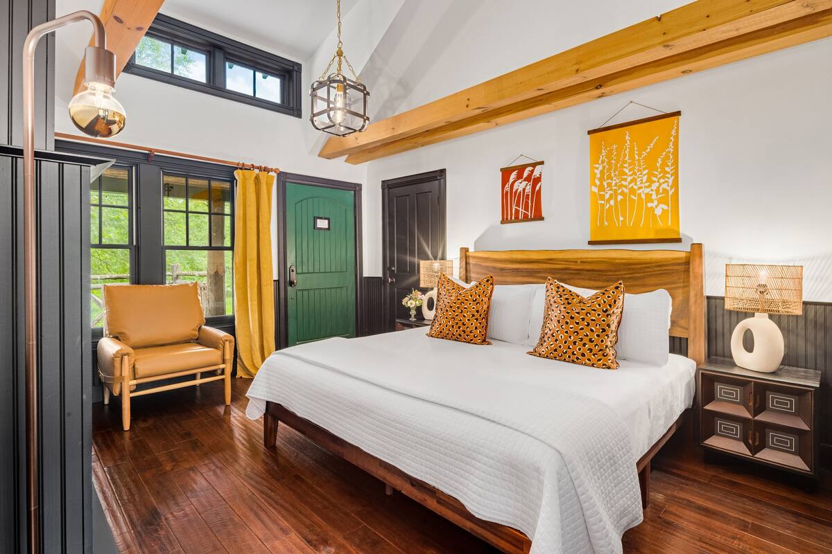 A spacious bedroom with a large bed, wooden headboard, and a view of the outdoors through a green door.