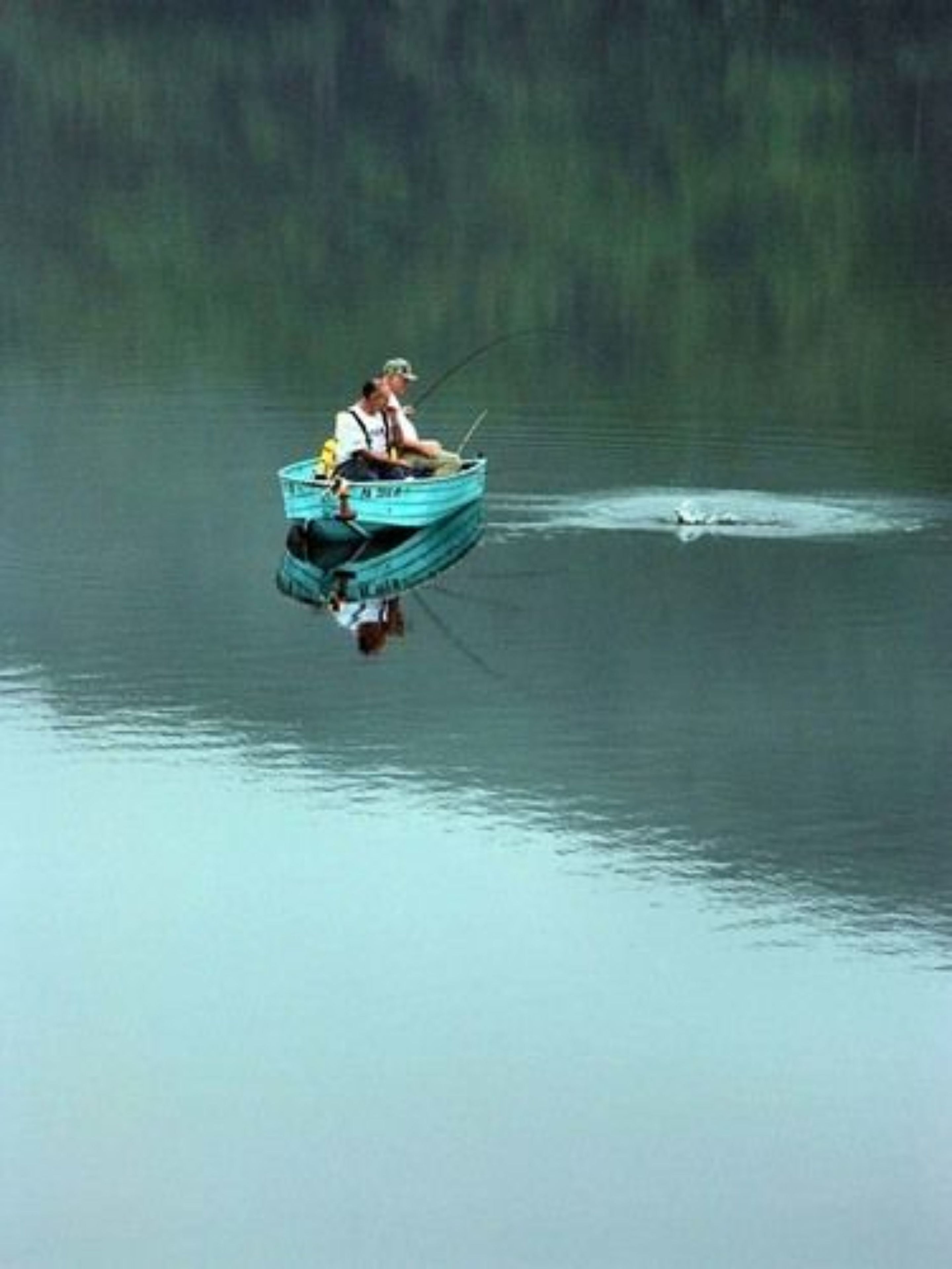 Una pequeña embarcación con dos personas pescando en un lago tranquilo.