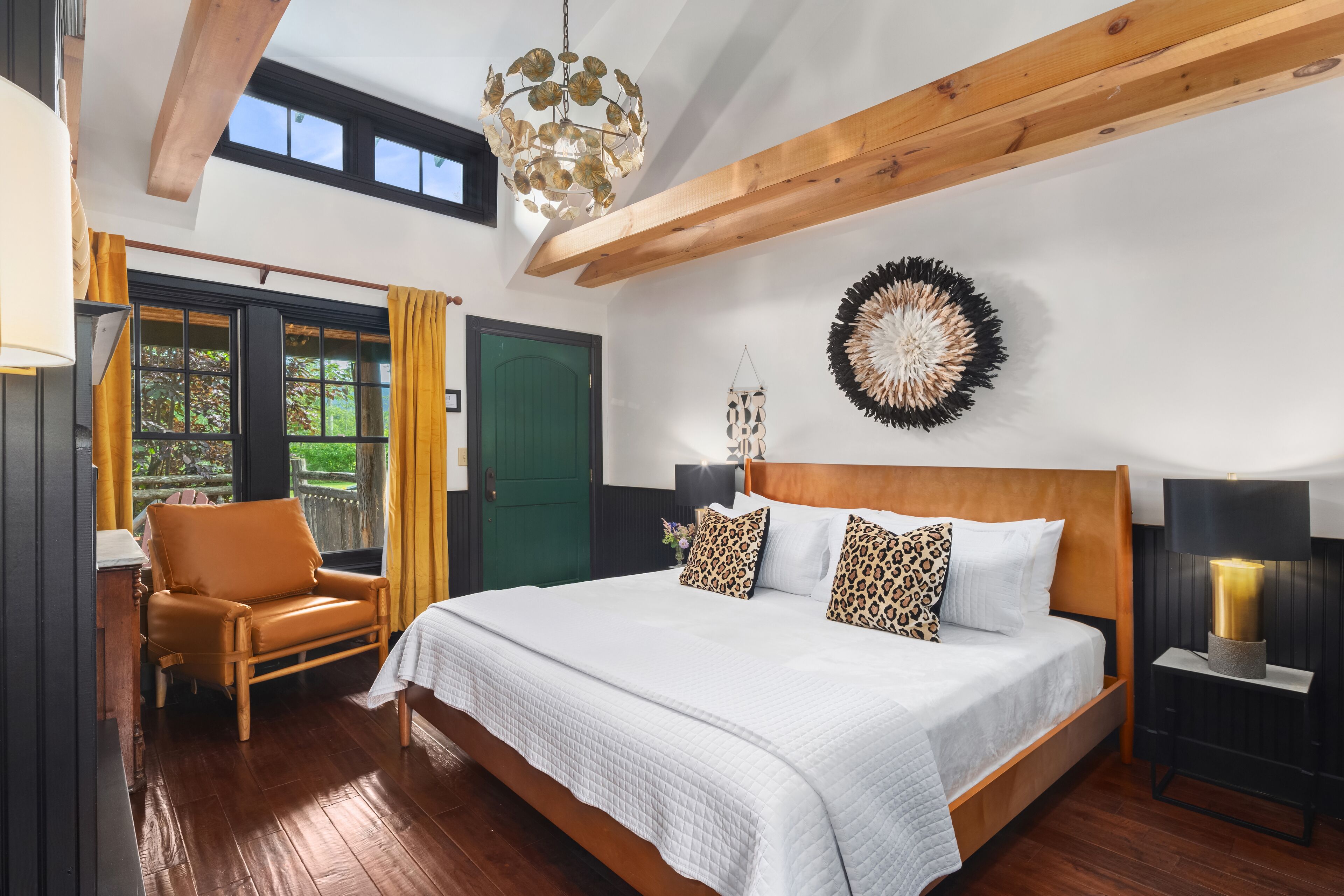 Un dormitorio con una cama grande, vigas de madera, una puerta verde y vistas al exterior.