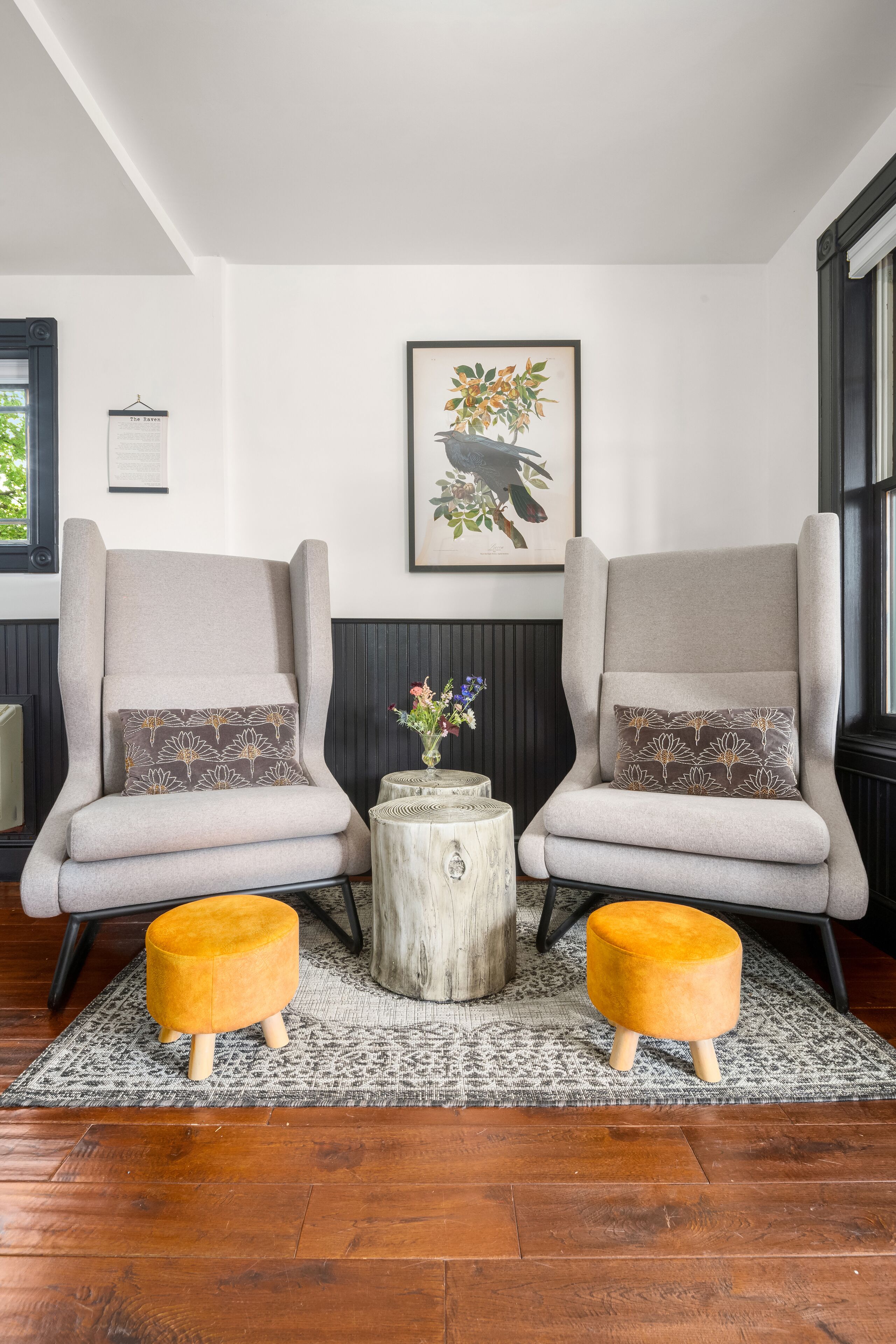 Twee fauteuils met bijpassende kussens, een klein houten bijzettafeltje met een vaas, en een tapijt met patroon op een houten vloer.
