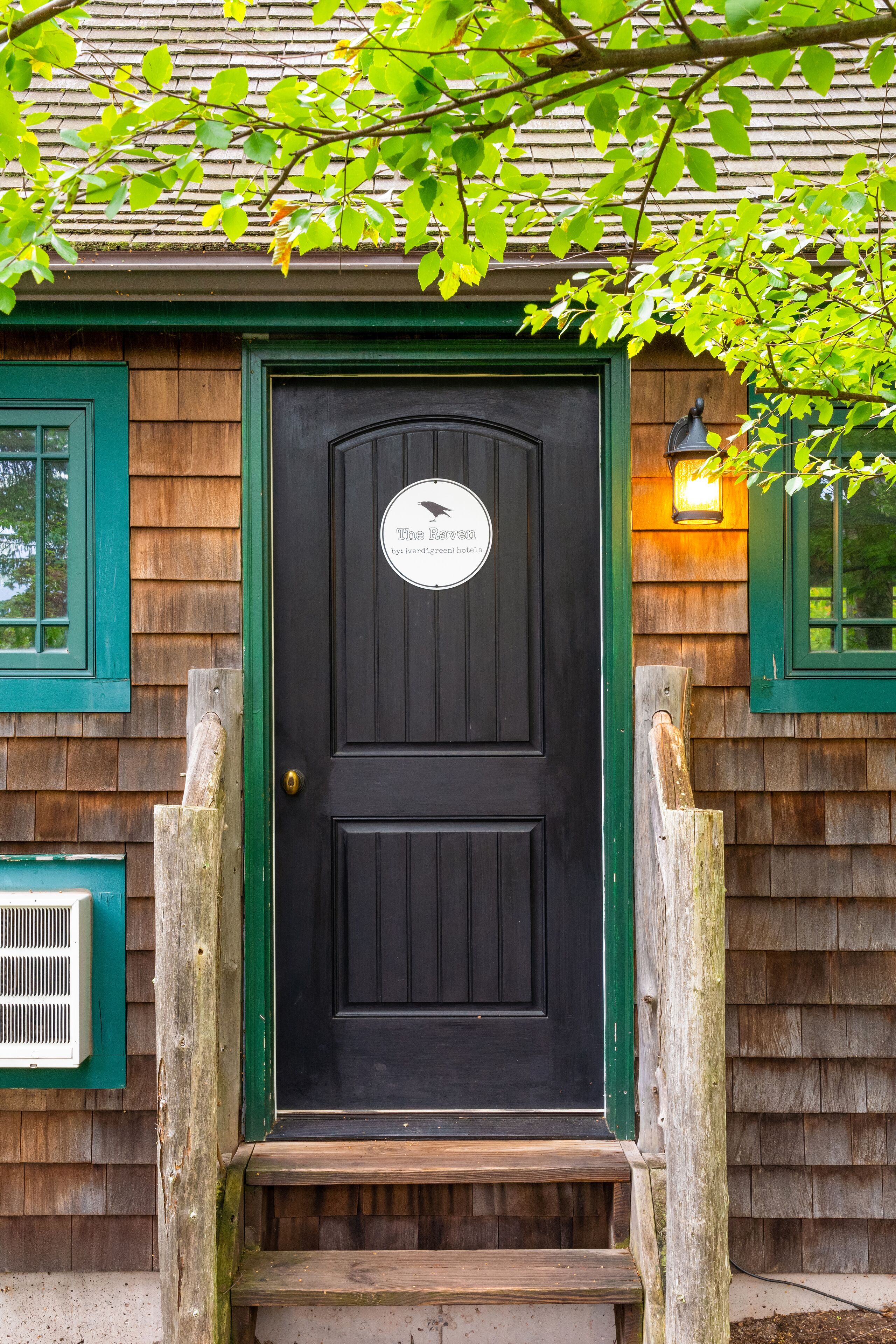 A black door with a sign, wooden steps, and a window with a green frame.
