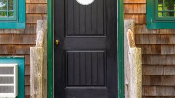 A black door with a sign, wooden steps, and a window with a green frame.