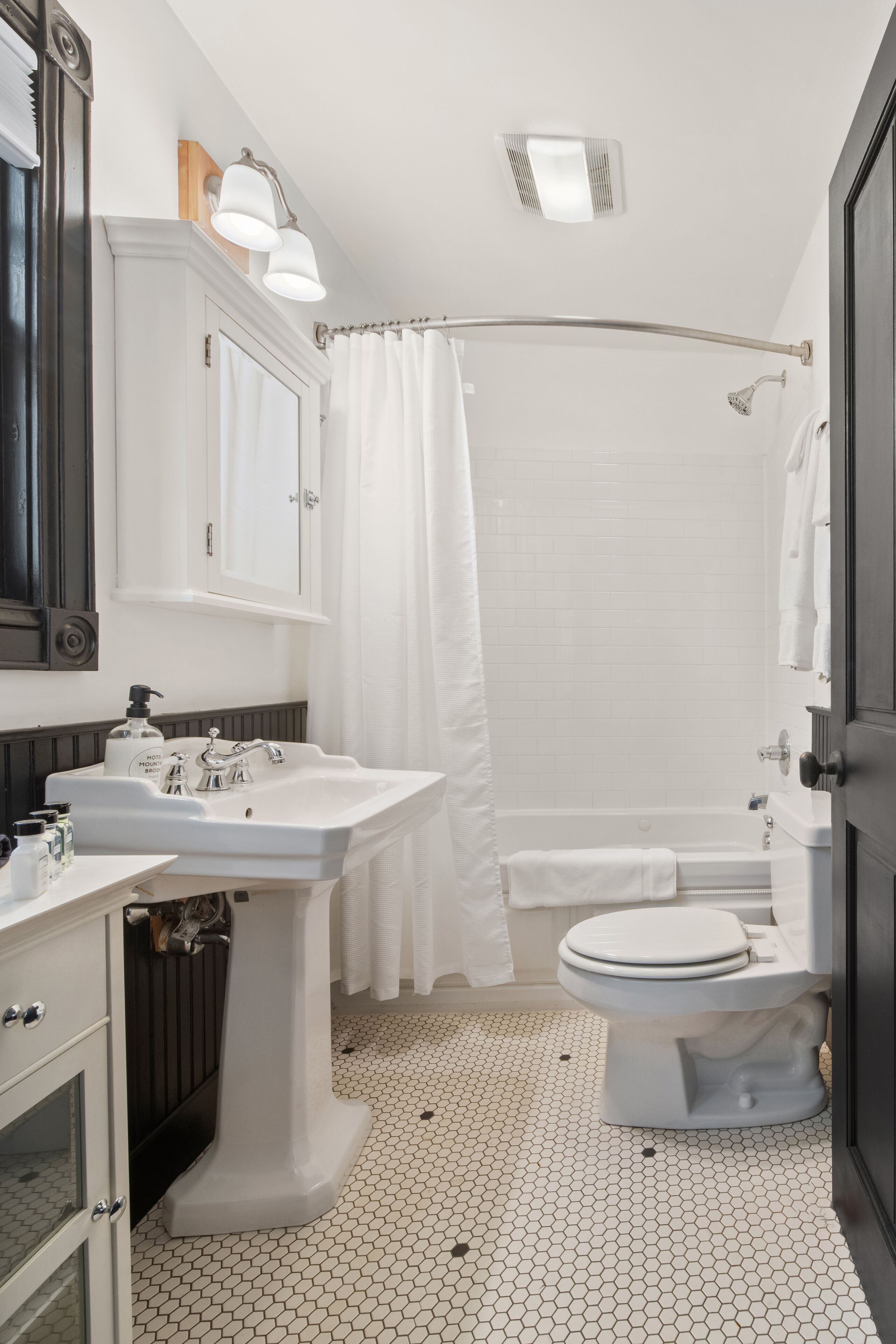 A bathroom with a white sink, toilet, and bathtub, featuring a tiled floor and a shower curtain.