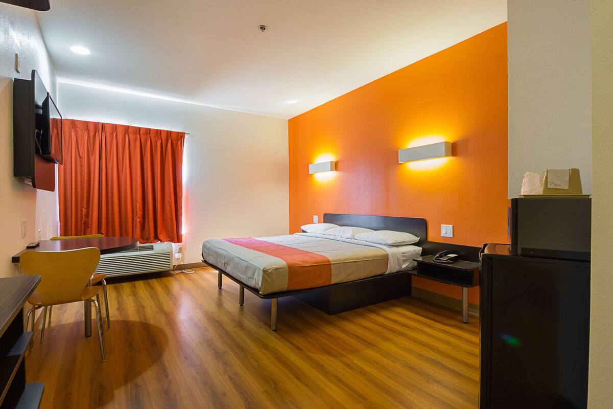 A hotel room with a bed, a desk, a chair, a television, and a refrigerator.