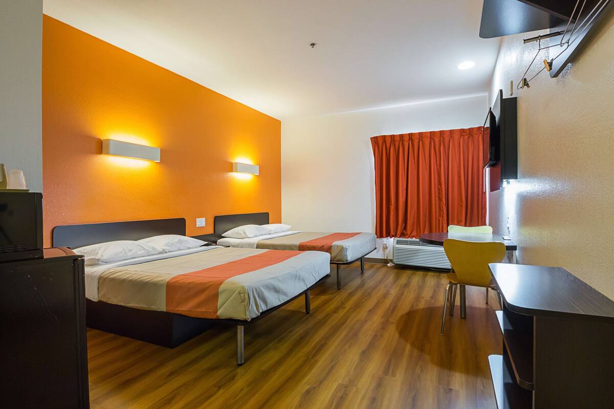 A hotel room with two beds, a desk, a chair, and a TV.