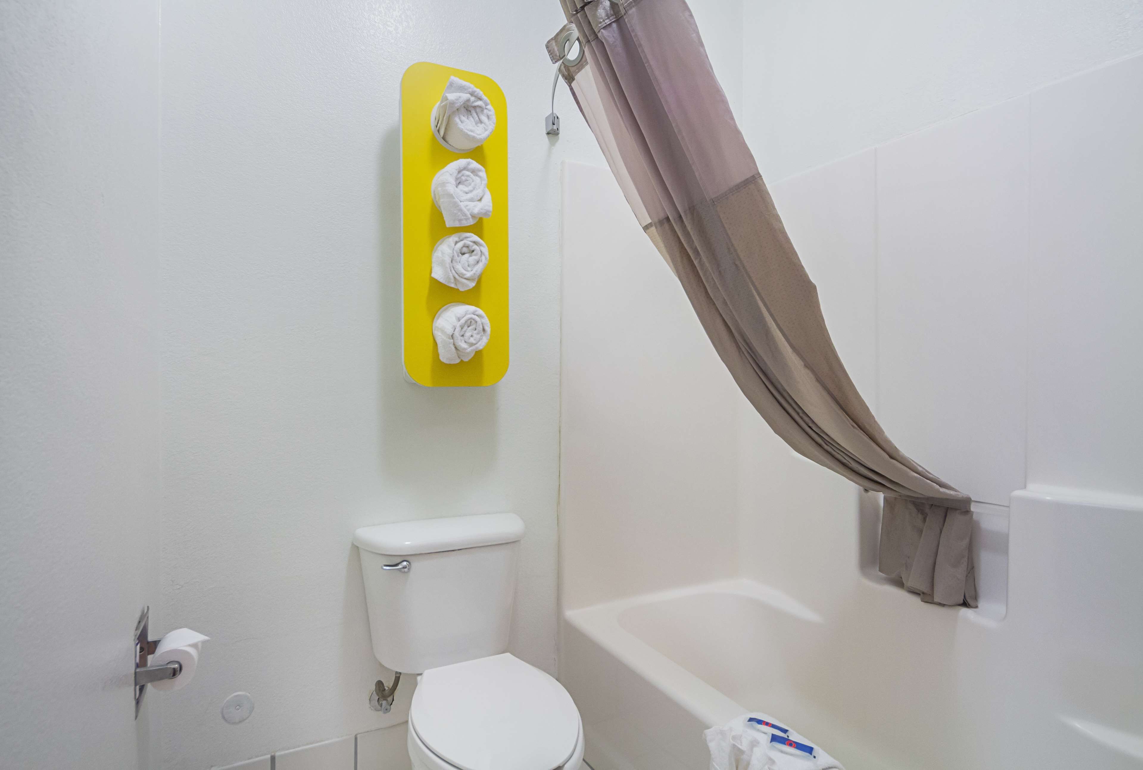 Un baño con inodoro, un toallero amarillo con cuatro toallas, cortina de ducha y bañera.