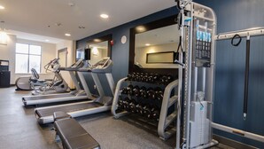 Un gimnasio con cintas de correr, una banca y un estante con mancuernas.