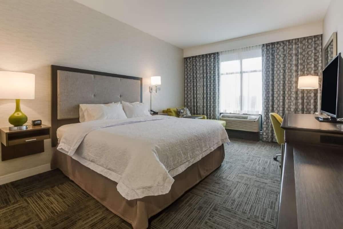 A hotel room with a large bed, a desk, a chair, a television, and a window with curtains.