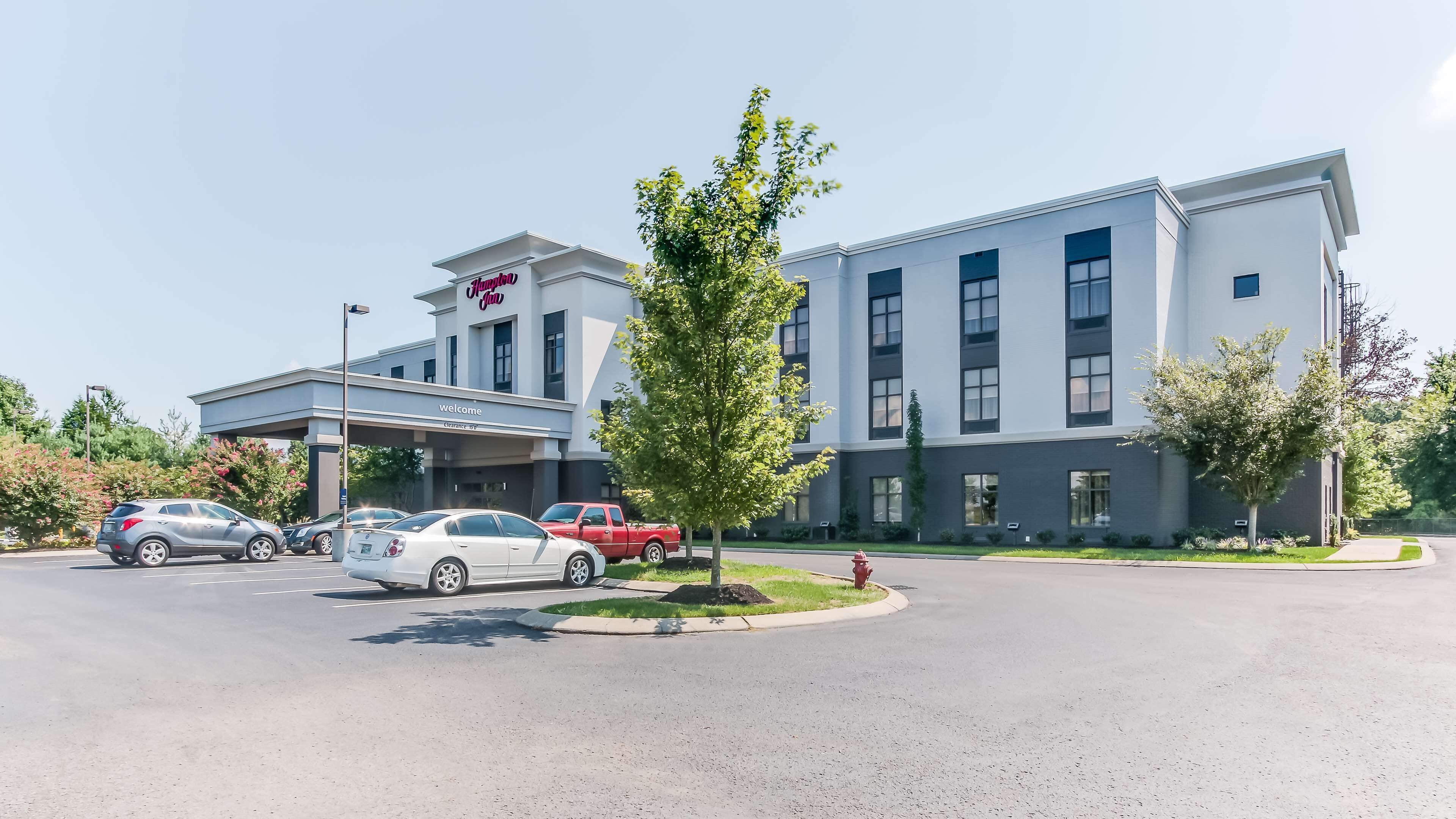 A modern hotel with a clear entrance, a parking lot, and a few cars parked in front.
