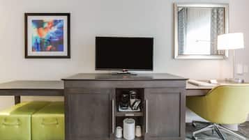 Habitación de hotel con un escritorio de madera oscura, un televisor de pantalla plana, una maleta verde, un sillón amarillo y un cuadro abstracto enmarcado.