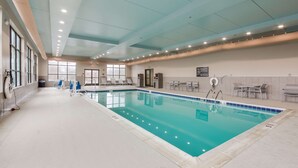 Una gran piscina interior con agua cristalina, rodeada por un solado de baldosas e iluminación empotrada en el techo.