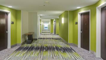 A hotel corridor with green walls, a patterned carpet, and doors marked with room numbers.
