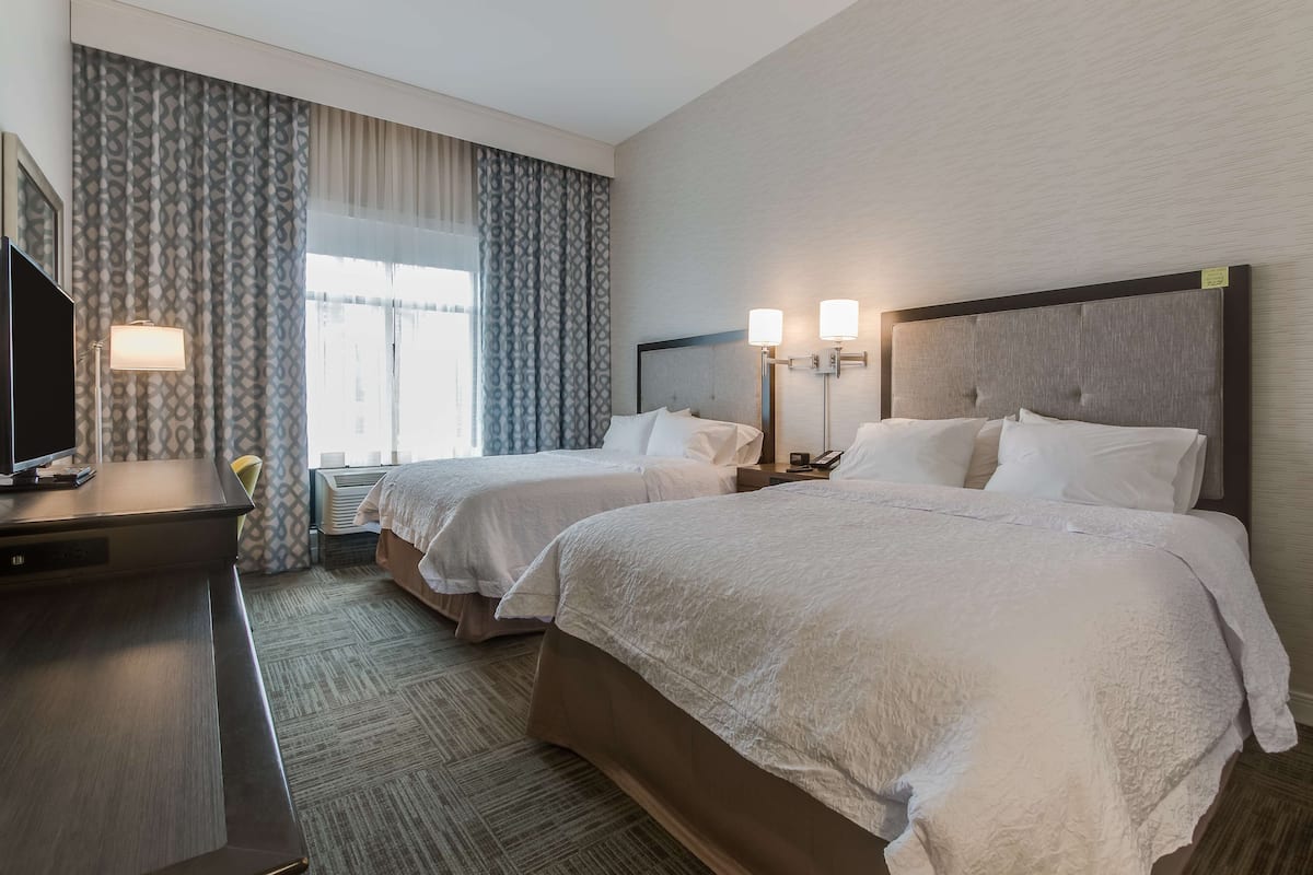 A hotel room with two beds, a desk with a TV, and a window with curtains.