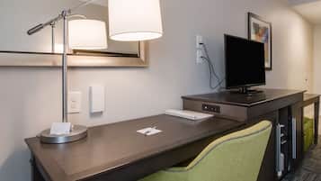Una habitación de hotel con un escritorio de madera, una lámpara, un televisor de pantalla plana y una silla verde.