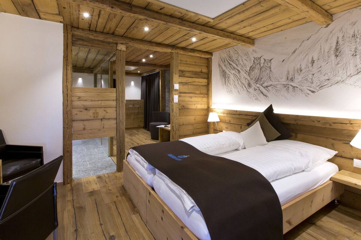 A wooden room with a bed, a desk, and a large wall painting.