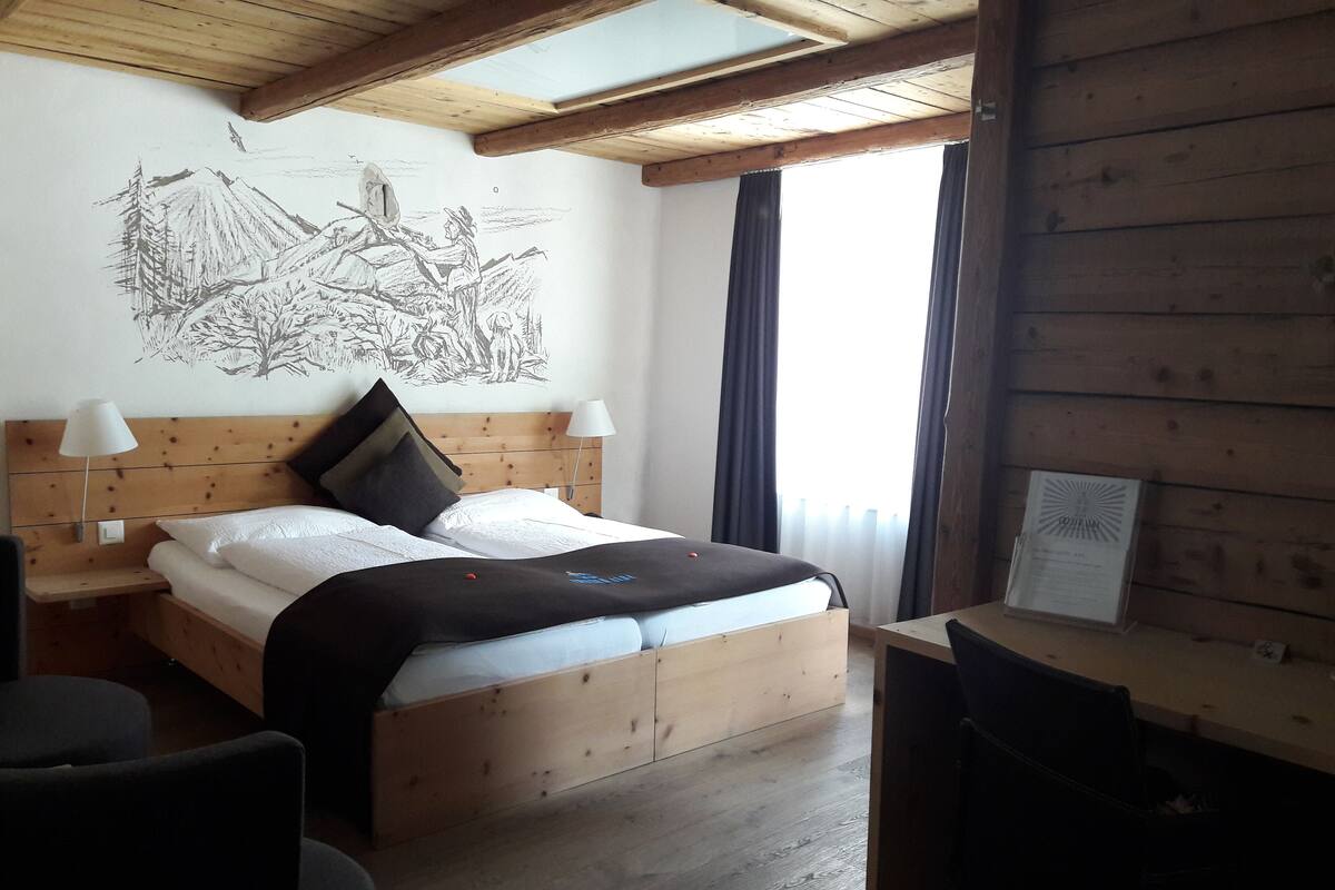 A wooden-framed bedroom with a bed, two bedside lamps, a desk, and a wall mural.