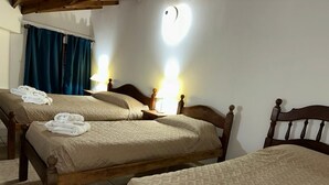 A hotel room with two wooden beds, each with a beige quilt and white towels. There are two bedside tables with lamps.