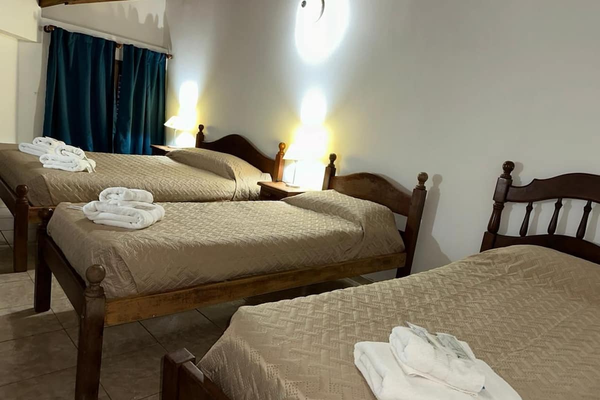 Une chambre d’hôtel avec deux lits en bois, chacun recouvert d’une couette beige et agrémenté de serviettes blanches. Il y a deux tables de chevet avec des lampes.