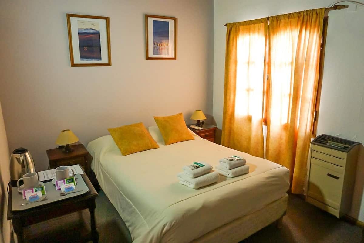 Une chambre d’hôtel avec un lit, deux oreillers, une table de chevet avec une lampe, une machine à café et une petite table sur laquelle se trouve un plateau avec des serviettes.