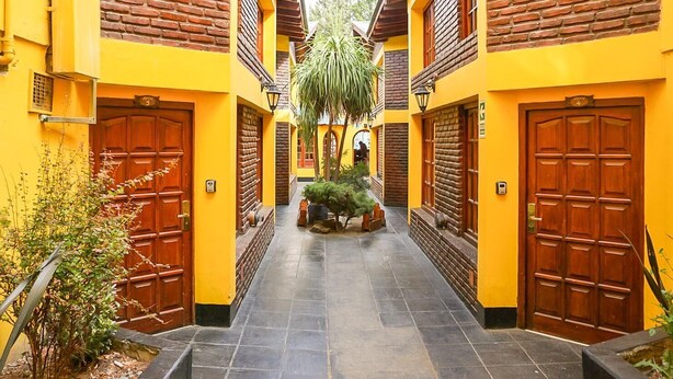 A narrow alleyway with yellow walls and wooden doors, leading to a central courtyard with a palm tree and potted plants.