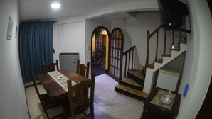 A dining area with a wooden table and chairs, a small refrigerator, and a staircase leading to an upper level.