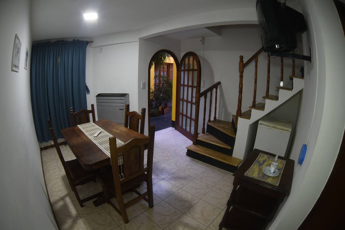 Un coin repas avec une table et des chaises en bois, un petit réfrigérateur et un escalier menant à un niveau supérieur.
