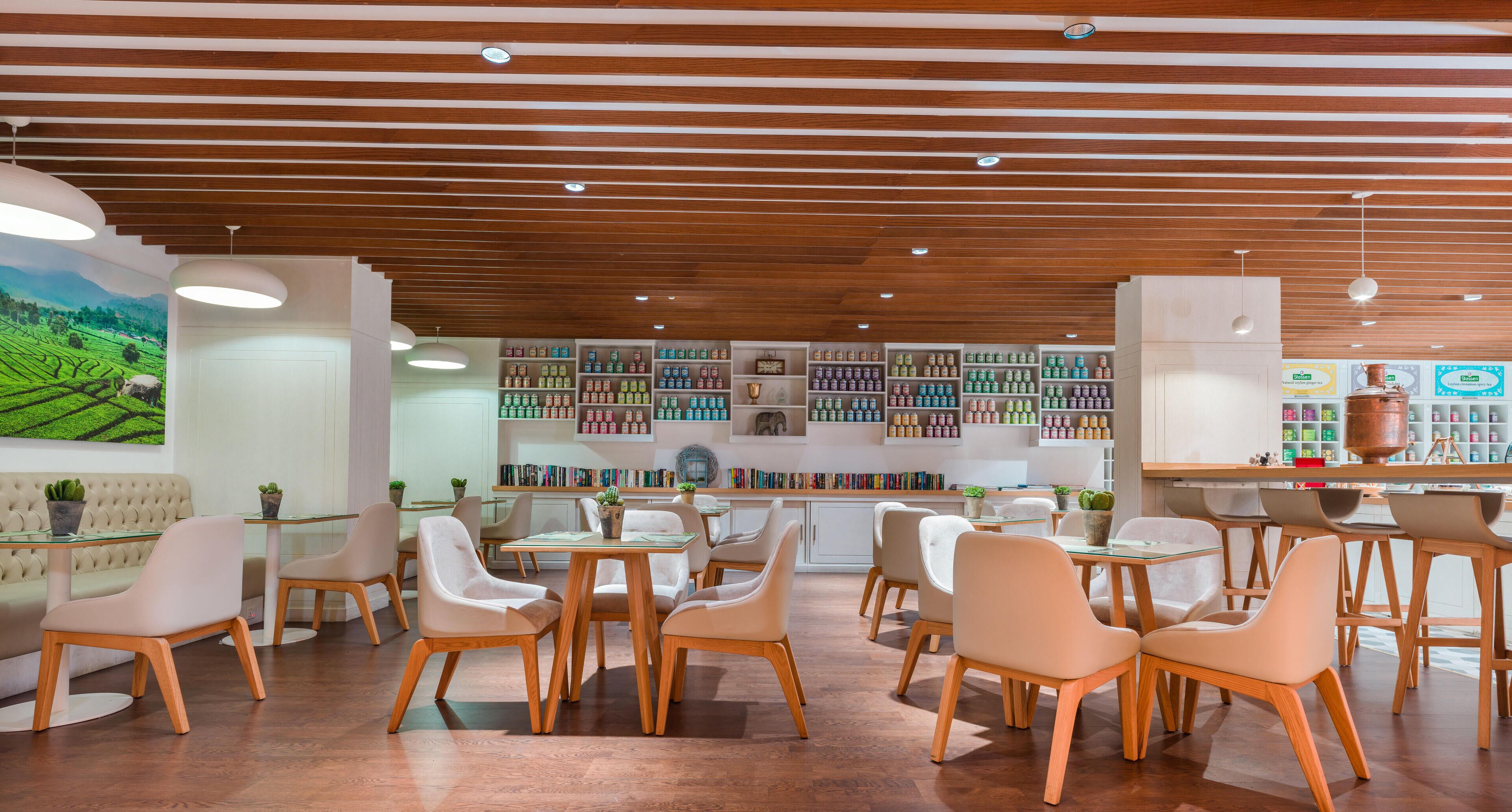 Un intérieur moderne avec un plafond en bois, des tables en verre et des chaises blanches. On peut apercevoir, au fond, des étagères remplies de divers objets.