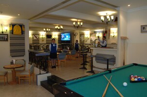A billiards room with a pool table, chairs, and a bar area.