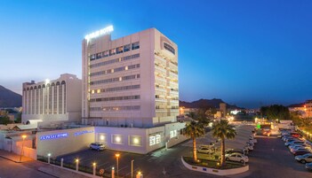 A multi-story hotel with a prominent sign, a parking lot, and a mountainous backdrop.
