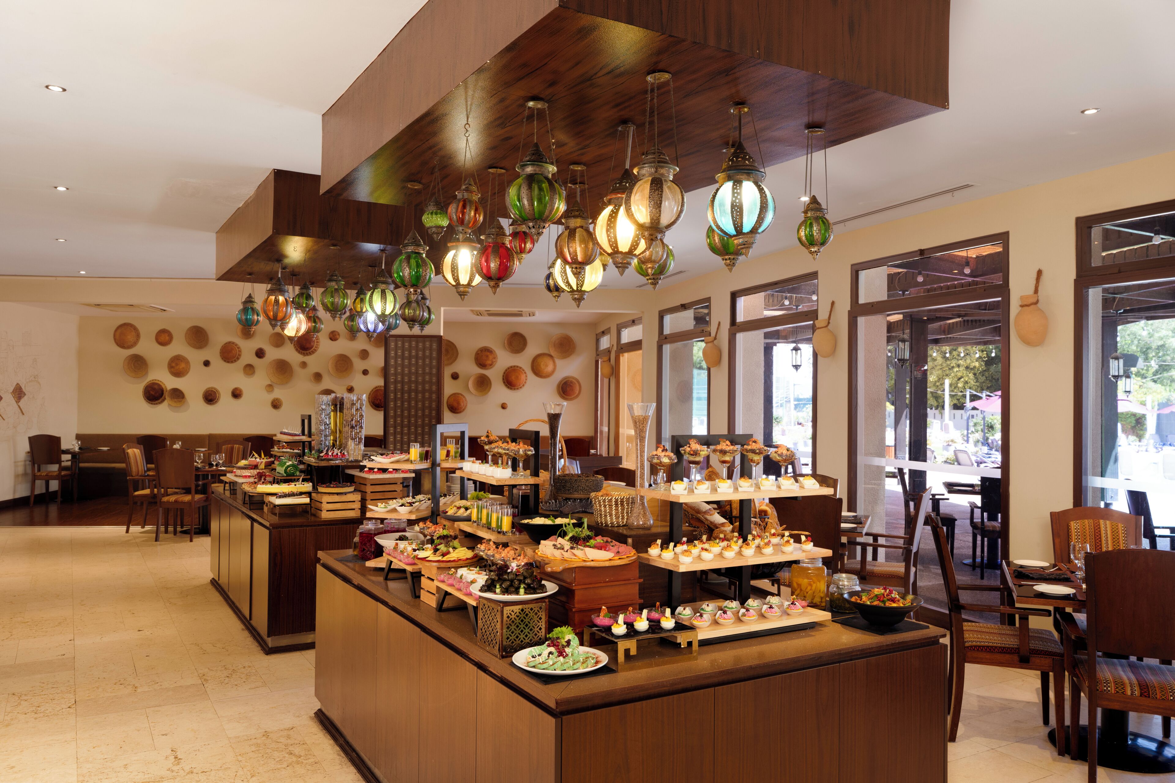 Zona de bufé con una variedad de alimentos, mobiliario de madera e iluminación decorativa colgante.