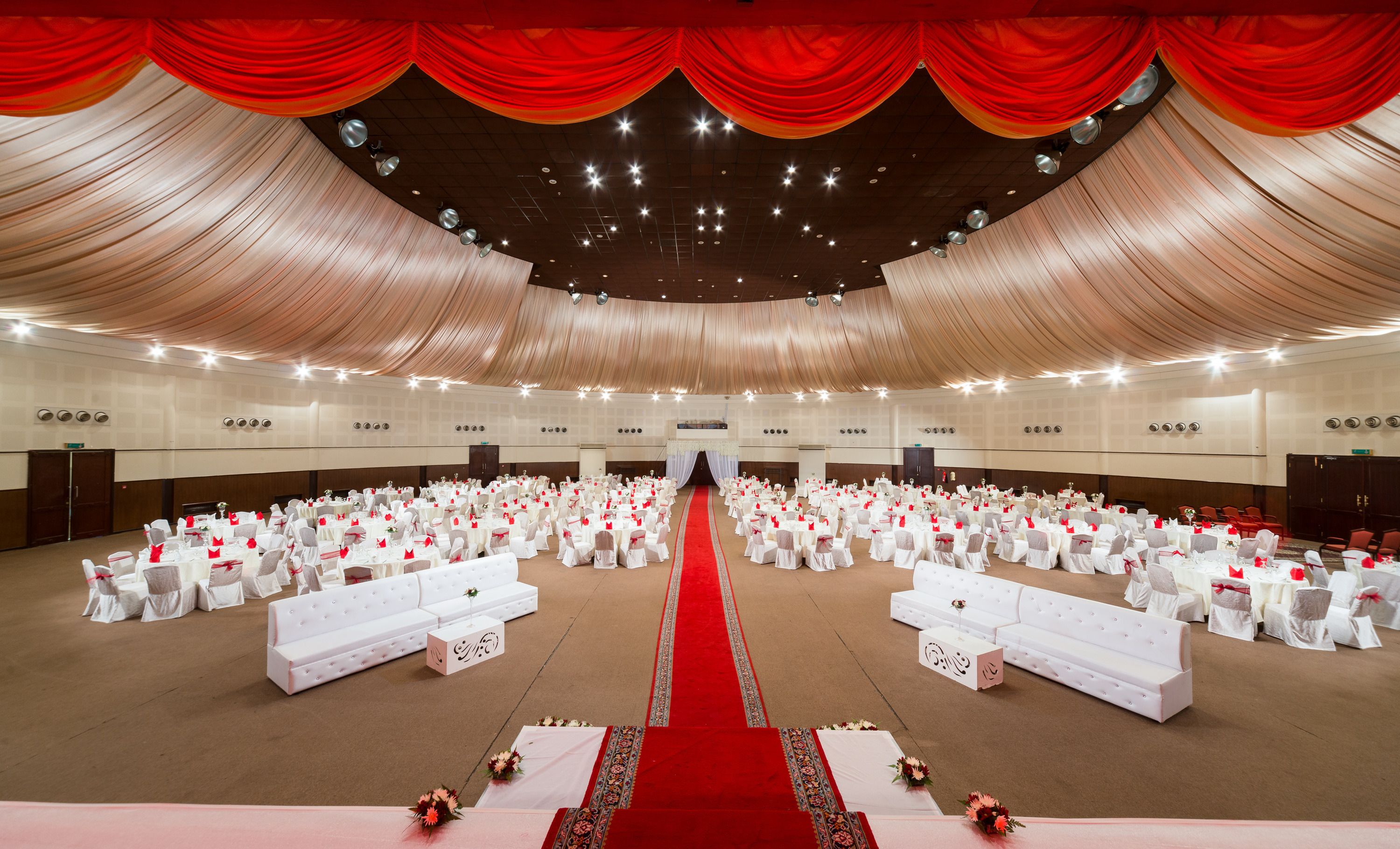 A large hall with rows of tables and chairs, a central aisle, and red drapery.