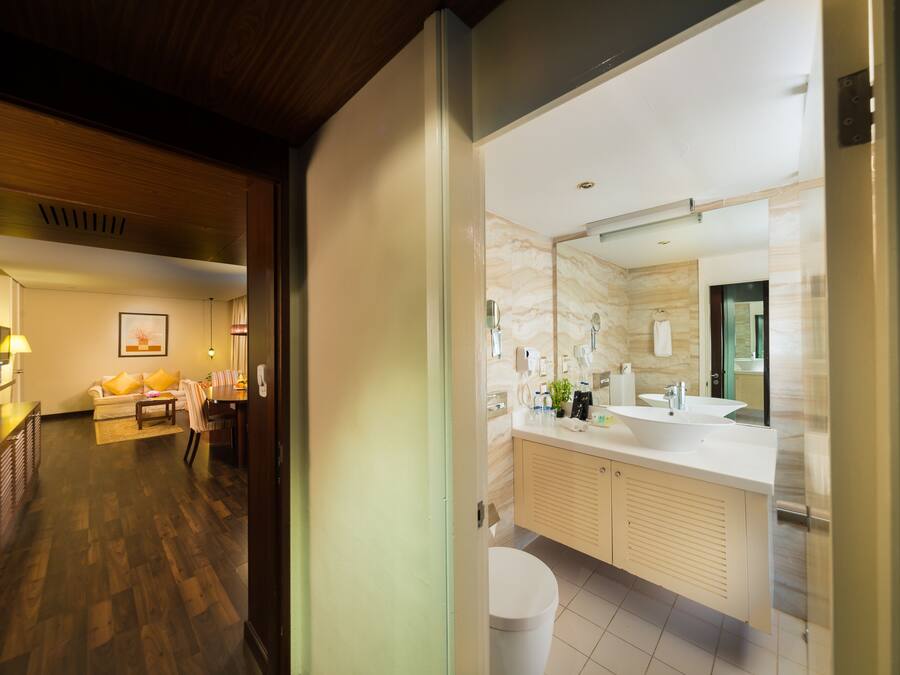 Un baño moderno con un espejo grande, un lavamanos blanco y armarios color beige.