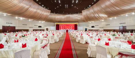 A banquet hall with rows of round tables, white tablecloths, and red centerpieces.