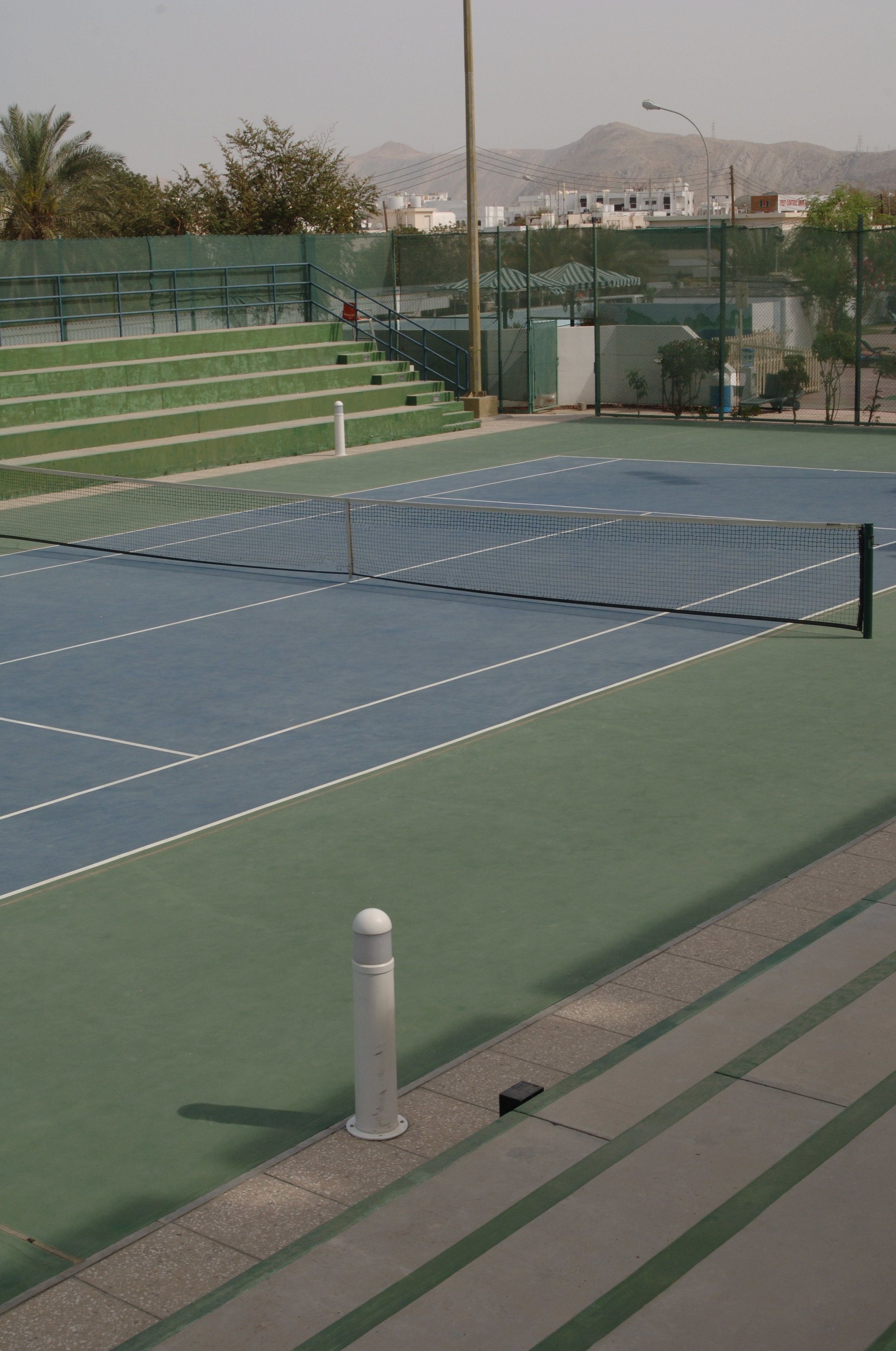 A tennis court with green and blue surfaces, a net, and surrounding fencing.