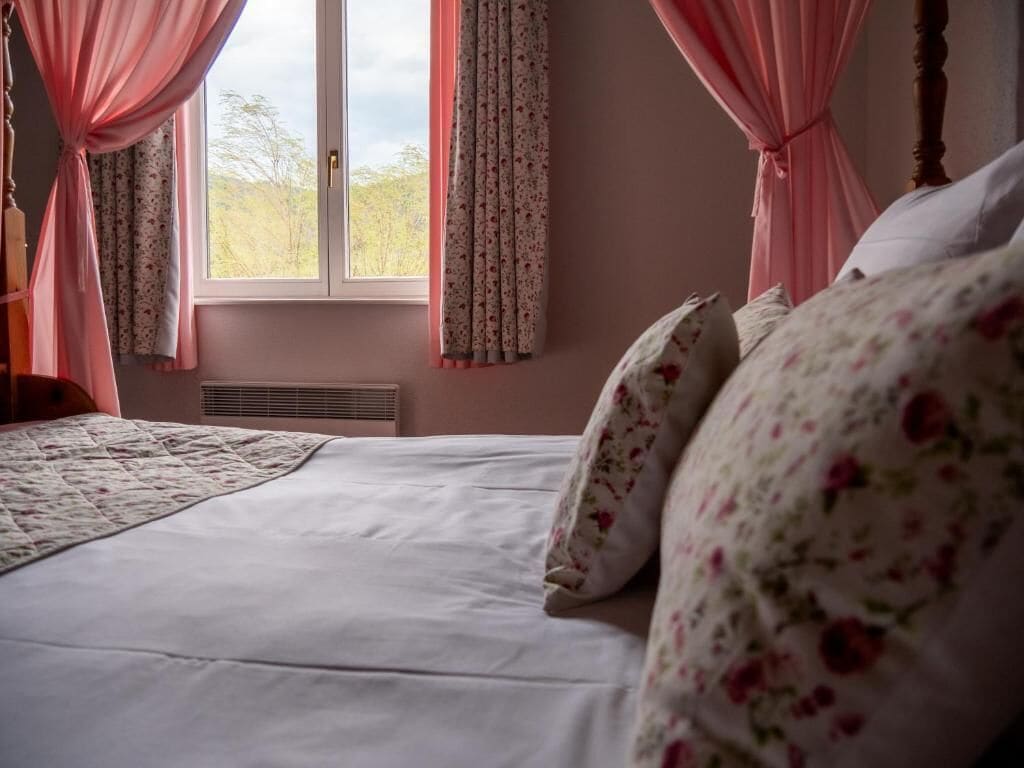 Ein Bett mit Blumenmuster auf der Bettwäsche, ein Fenster mit Vorhängen und eine Heizung.