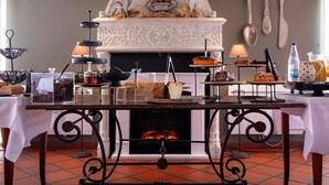 A dining area with a fireplace, a variety of food and drink items on tables, and a decorative bird sculpture above the mantel. - The Originals Relais, Le Verger des Châteaux (Dieffenthal)