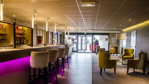 Un espace bar moderne avec un comptoir illuminé de lumière violette, des tabourets de bar et des chaises jaunes.