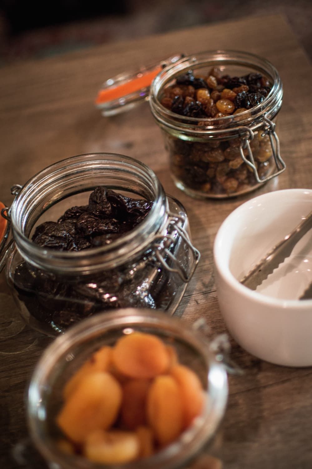 Three glass jars with metal lids containing dried fruits on a wooden surface.