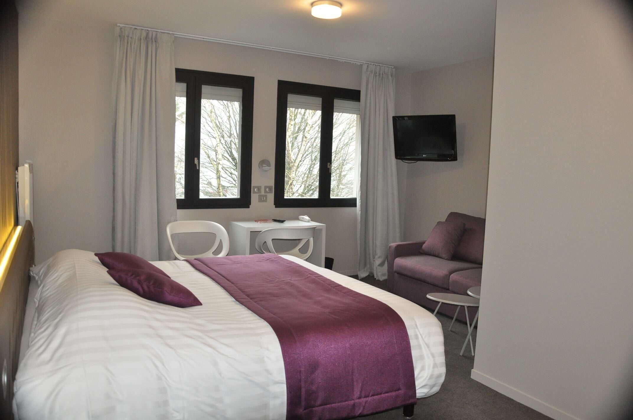 Habitación de hotel con cama, dos sillones, una mesita, un sofá y televisión fijada a la pared.